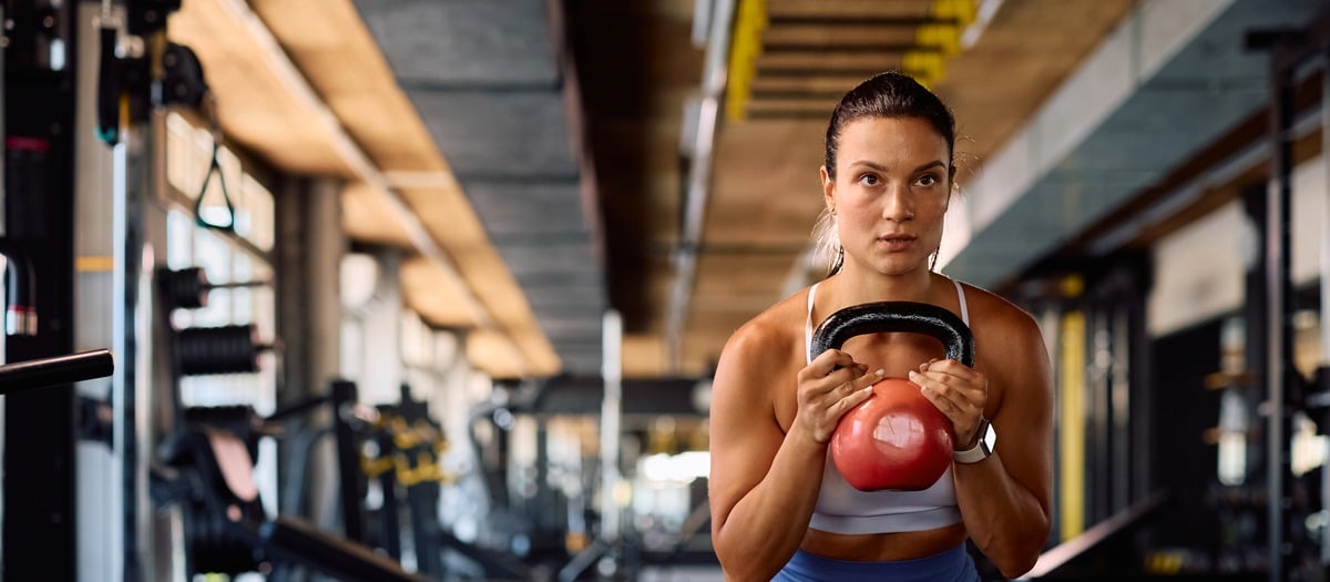 Woman performing a kettlebell squat during a personal training session in a gym