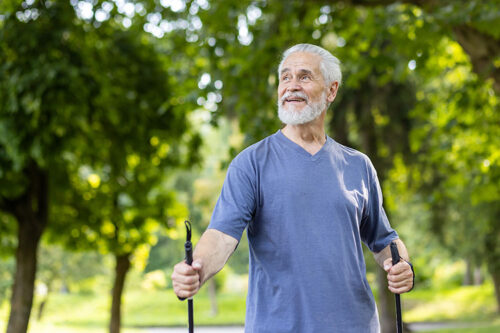 Older man walking outdoors with walking sticks