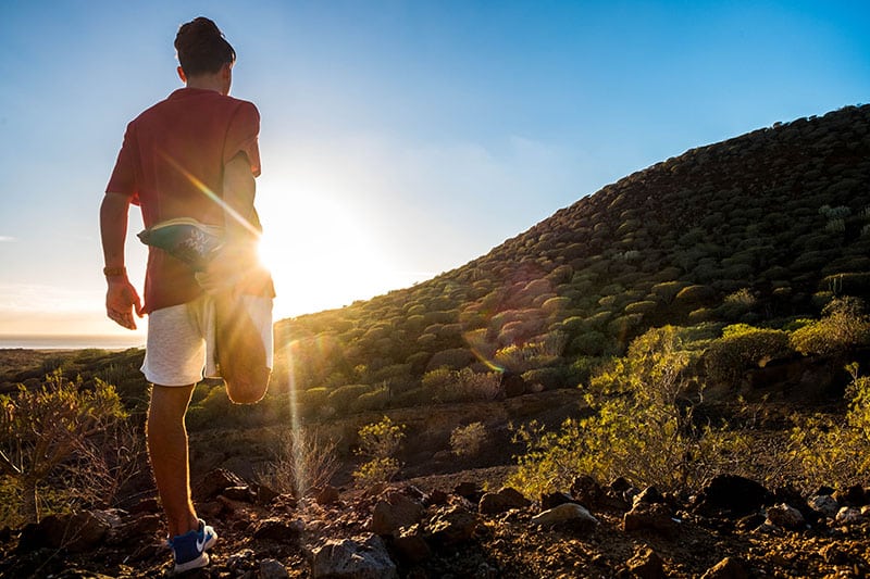 Runner stretching on hill at sunset
